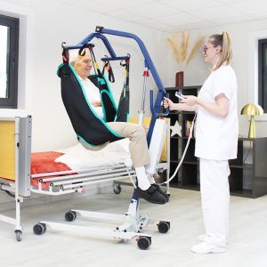 Grúa compacta FLY 4 Compact elevando a un paciente desde la cama con arnés de traslado en posición sentada