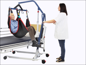 Grúa compacta FLY 4 Compact realizando transferencia de paciente desde la cama con arnés, en posición sentada y segura