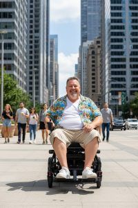 Usuario en silla eléctrica bariátrica plegable Optima Plus circulando por acera en entorno urbano