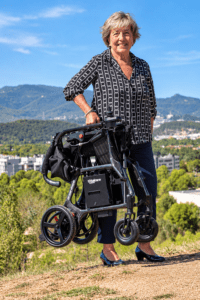 Mujer transportando con una mano la silla eléctrica Martinika Carbon Evo plegada en un entorno exterior